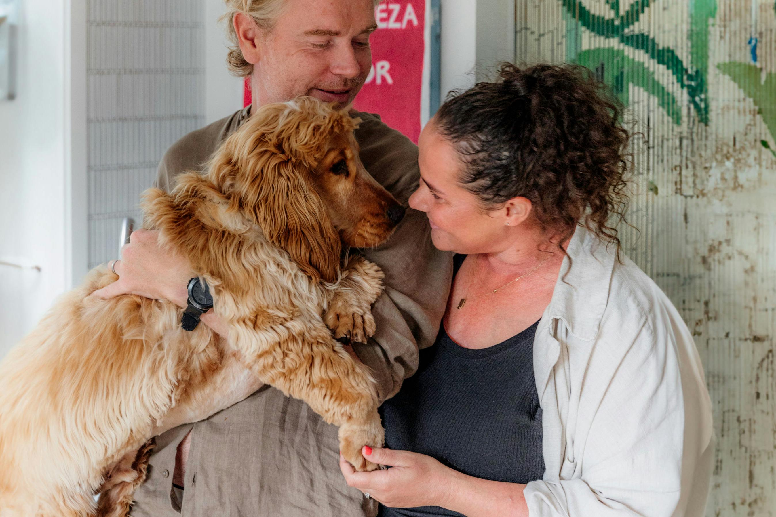Couple smile and hold up their dog in their home